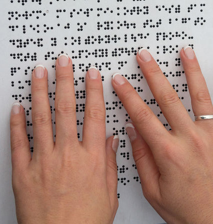 Photographie des doigts d'une femme lisant une page en braille