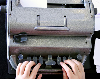 Photographie avec vue sur les doigts d'une personne tapant sur une machine à écrire en braille Perkins.