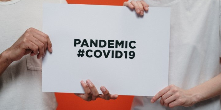 Photo of two people holding a sign reading, 'Pandemic #covid19'