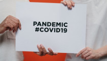 Photo of two people holding a sign reading, 'Pandemic #covid19'